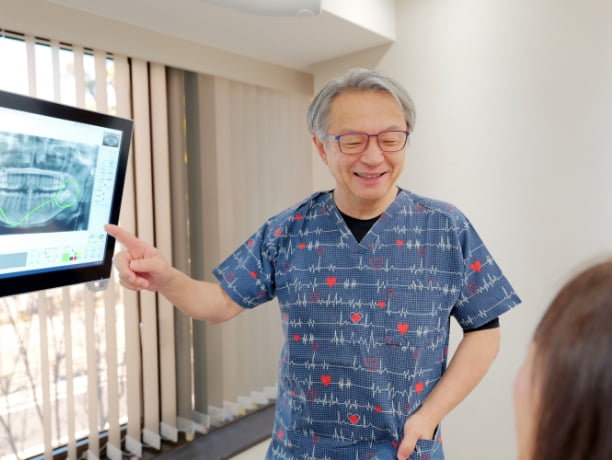 モニターにうつるレントゲン写真を指差しながら話す歯科医師